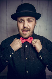 Portrait of man holding bow tie while standing against wall