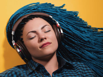 Close-up of young woman with braided hair listening to music against yellow background