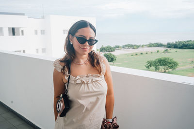 Portrait of young woman wearing sunglasses while standing against sea