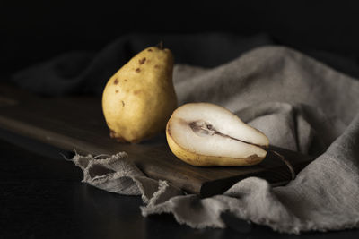 Aged pears on wooden board on linen, one cut, one whole