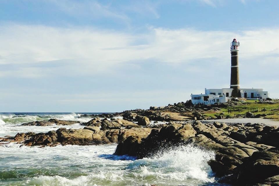 sea, water, sky, built structure, architecture, building exterior, lighthouse, horizon over water, rock - object, cloud - sky, wave, guidance, shore, beach, surf, scenics, nature, beauty in nature, day, cloud