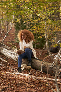 Woman reading book sitting on log in autumn forest