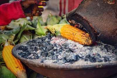 Close-up of person preparing corn on fire pit