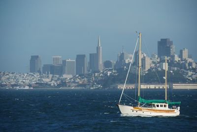 Sailboats in sea by buildings against clear sky