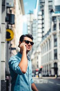 Young man wearing sunglasses standing against city