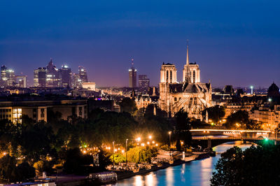 Illuminated buildings by river against sky at night