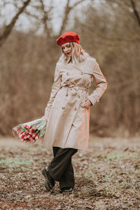 Full length of woman wearing trench coat holding bouquet standing in forest