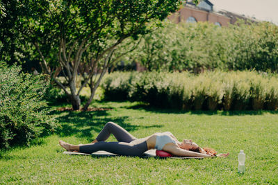 Side view of woman exercising on mat against trees in park