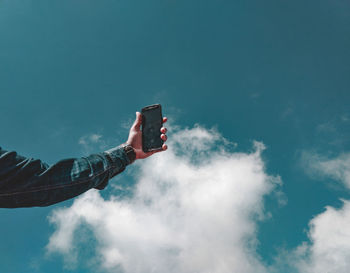 Low angle view of hand holding mobile phone against sky