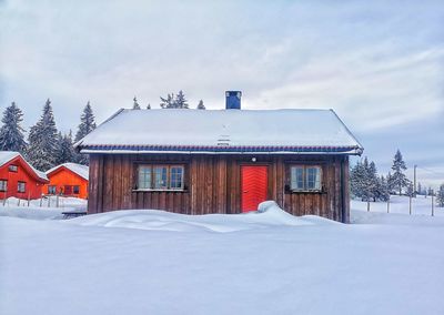 Houses on snow covered field by building against sky
