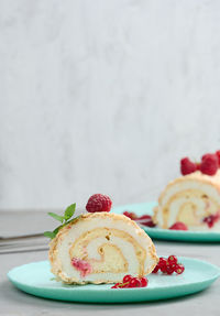 Baked meringue roll with red berries on a round plate, white background