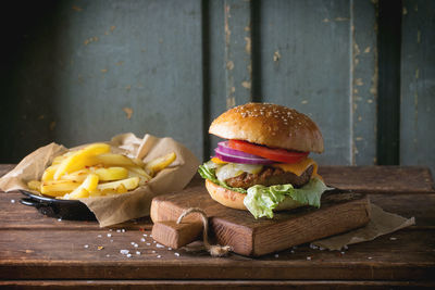 Burger with grilled potatoes on wooden table against old wall