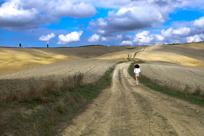 Rear view of man walking on road against sky