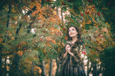 Woman in warm clothing standing against tree