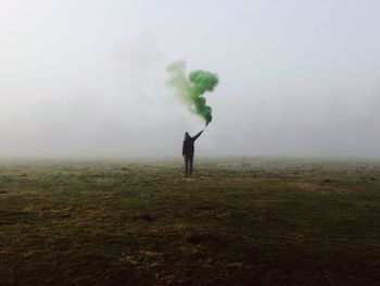 Rear view of man holding smoke bomb on field in foggy weather