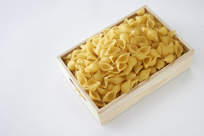 Close-up of raw pasta in crate against white background