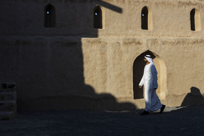 Side view of man wearing traditional clothing walking by old building