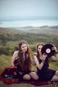 Two hippie woman are lying in a field on a mountain with an old gramophone on a vinyl record