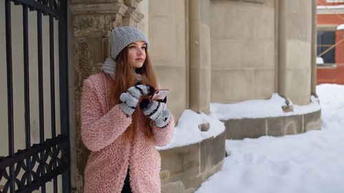 Young woman using phone while standing in snow