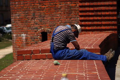 Full length of man sitting on brick wall