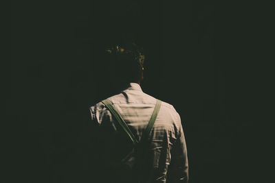 Rear view of man standing against black background