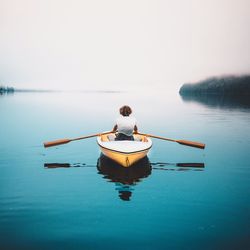 Rear view of woman in boat on sea against clear sky