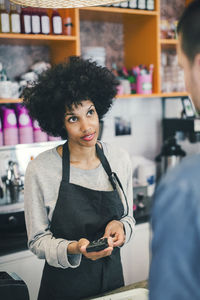 Barista using credit card reader to make payment while looking at customer in cafe