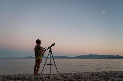 Man photographing at beach against clear sky during sunset