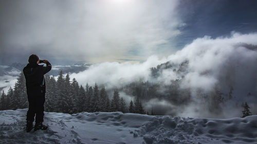 Man photographing on snow covered land against sky