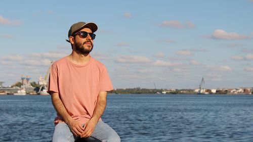 Man wearing sunglasses sitting by sea against sky