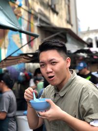 Portrait of young man eating food while standing on city street 