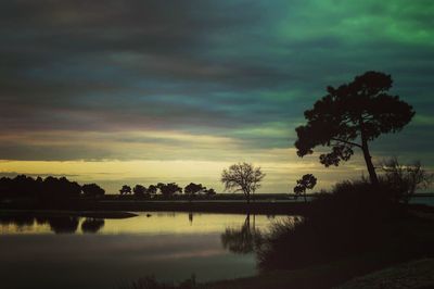 Silhouette trees by lake against sky during sunset