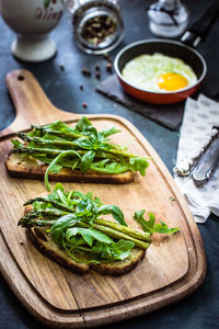 High angle view of asparagus with breads and arugula on cutting board