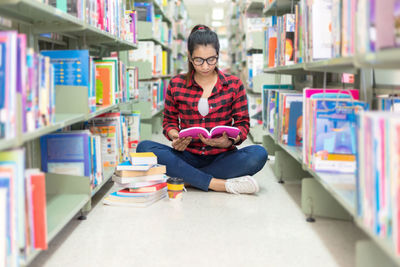 Woman reading book while sitting at bookshelf