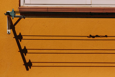 Bold shadow from the clothesline on the yellow wall of the house in a bright, summer day.