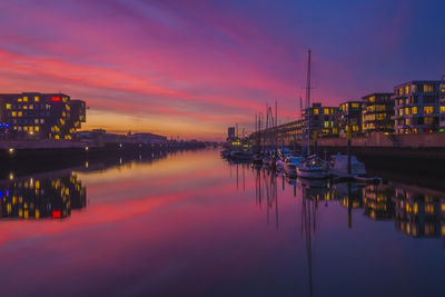 Illuminated buildings by river against sky during sunset