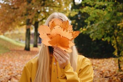 Portrait of person hiding behind autumn leaves, holding leaves in front of face