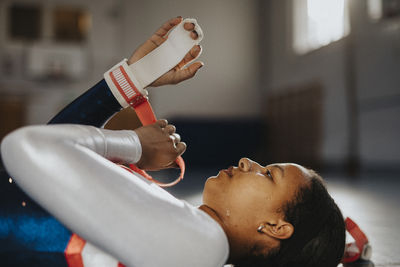 Female athlete adjusting protection band while lying on floor in gym