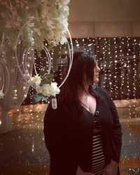 Young woman standing by illuminated flowering plants at night