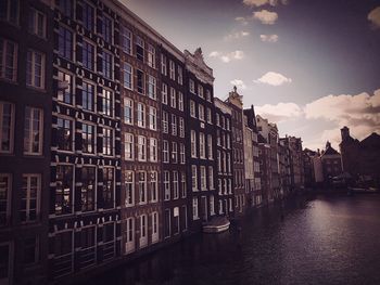 Buildings by canal against sky in city