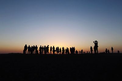 Silhouette people standing on field against clear sky during sunset