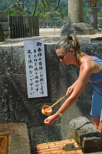 Side view of woman washing hand by wall