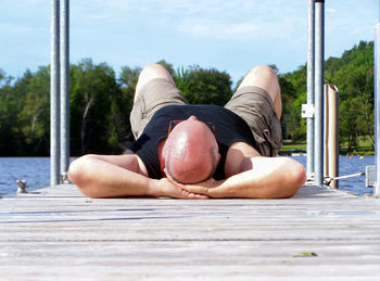 Man lying down on pier over lake against sky