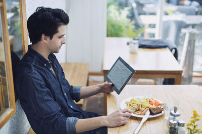 Man using digital tablet while having lunch at cafe