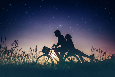 Silhouette people on bicycle over field against sky at night