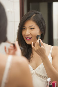 Beautiful woman using blusher brush while looking in the mirror