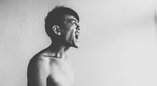 Aggressive young man screaming against white wall