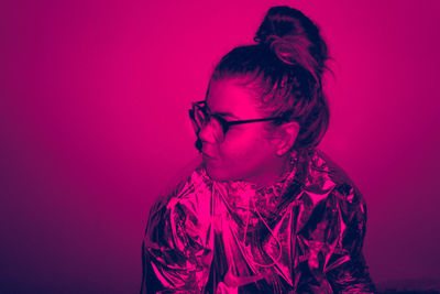 Portrait of young woman standing against pink wall