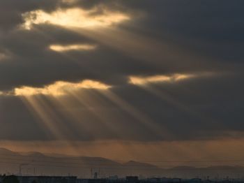 Low angle view of sunlight streaming through clouds during sunset