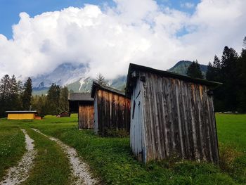 Barn on field by houses against sky